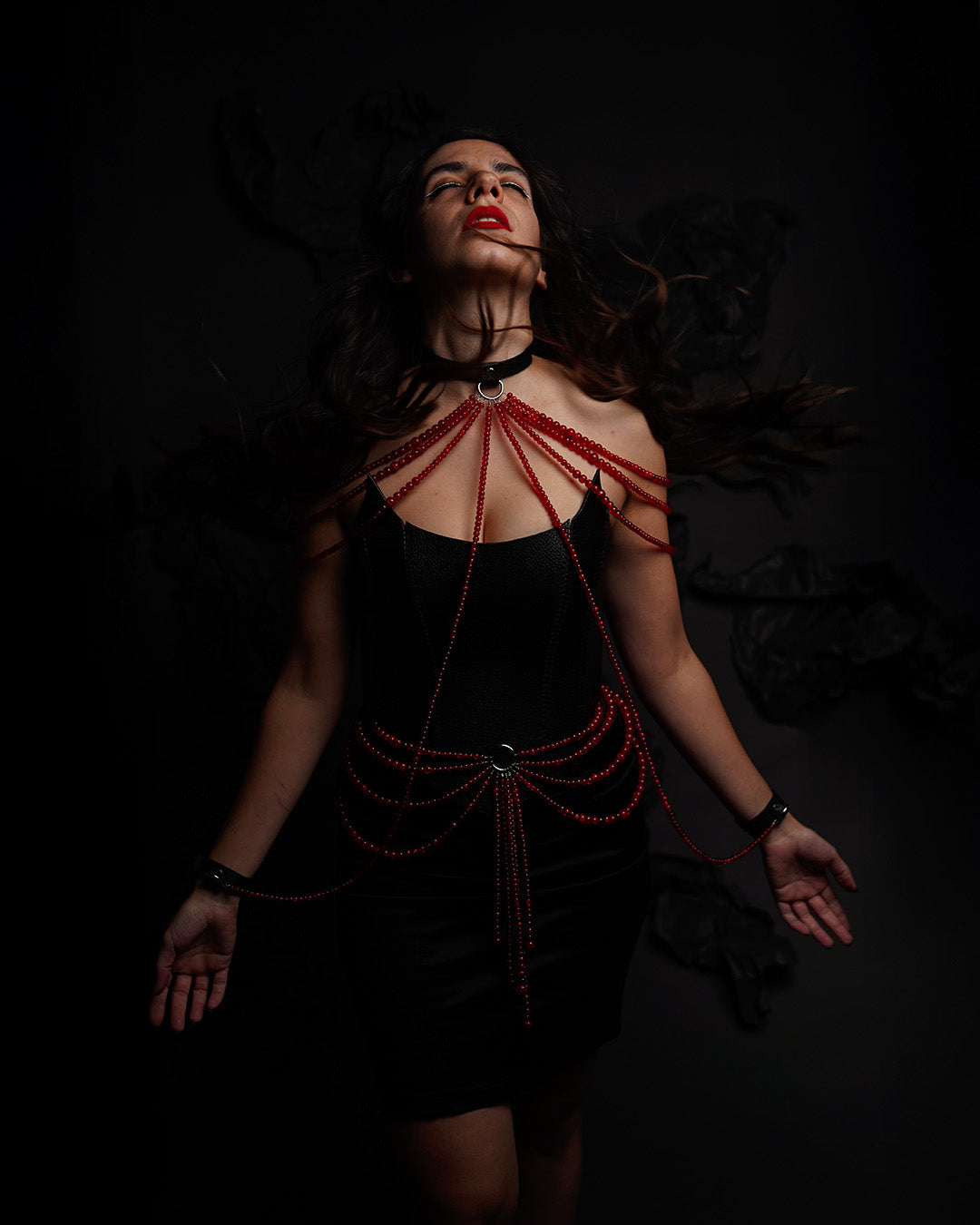 model wearing leather choker inspired by persephone with red beads chains draping on the shoulders and cuffs attached to the choker and a red beads belt with draping design